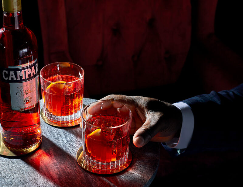 Two negroni cocktails with a bottle of Campari